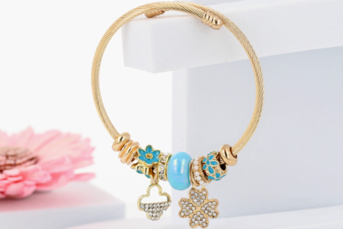 Złota bransoletka z zawieszkami – kwiatki, koniczynka i cyrkonie. Biżuteria damska ze stali szlachetnej.